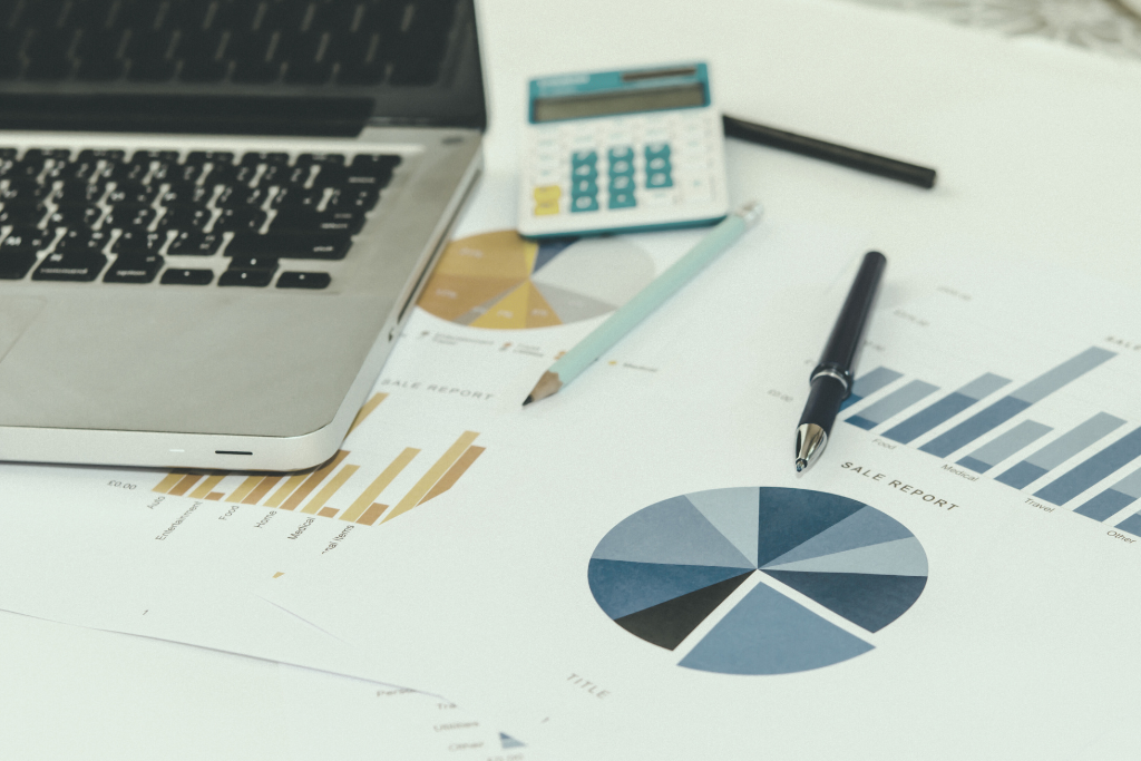 Calculator, laptop, and charts to calculate profit margins.